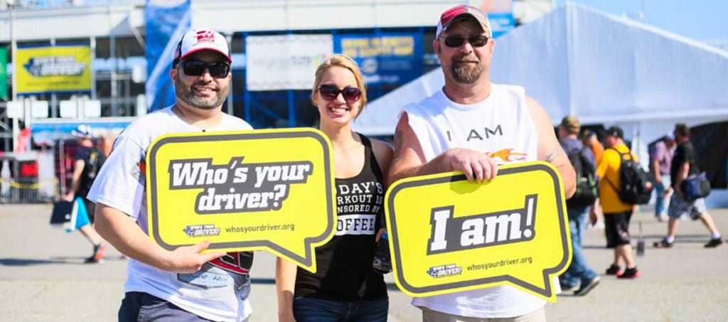 Race fans holding "Who's Your Driver" signage