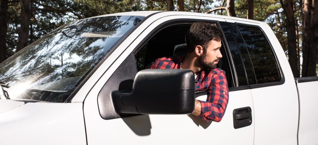 confident young handsome man sitting in pick up car and looking away in forest